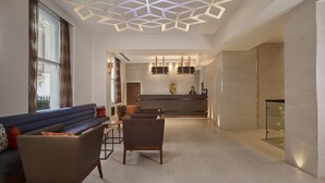 Eine moderne Hotelhalle mit Rezeption, Sitzgelegenheiten und einem geometrischen Deckenmuster.