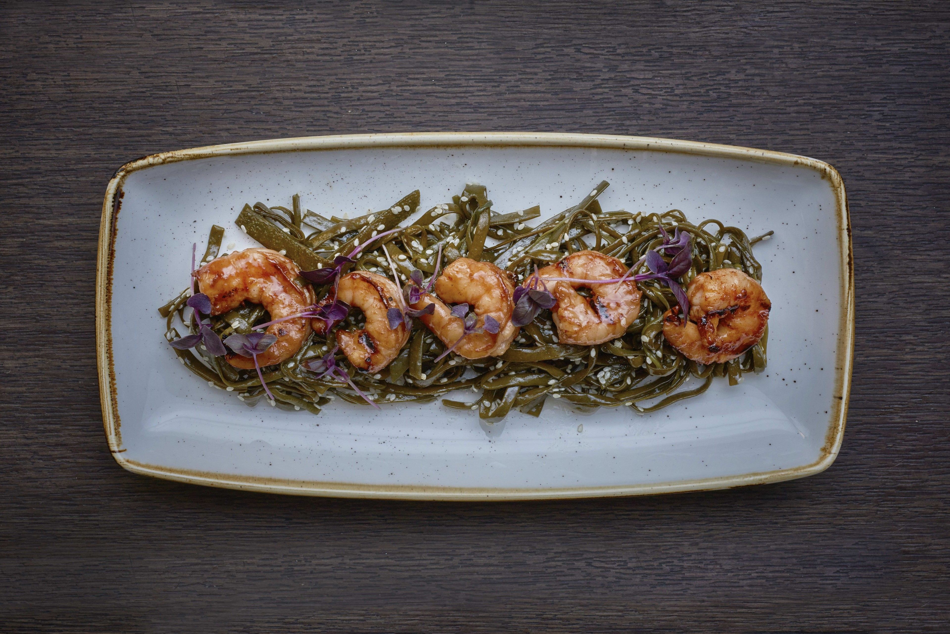 A rectangular plate with cooked shrimp and greens on a dark wooden table.
