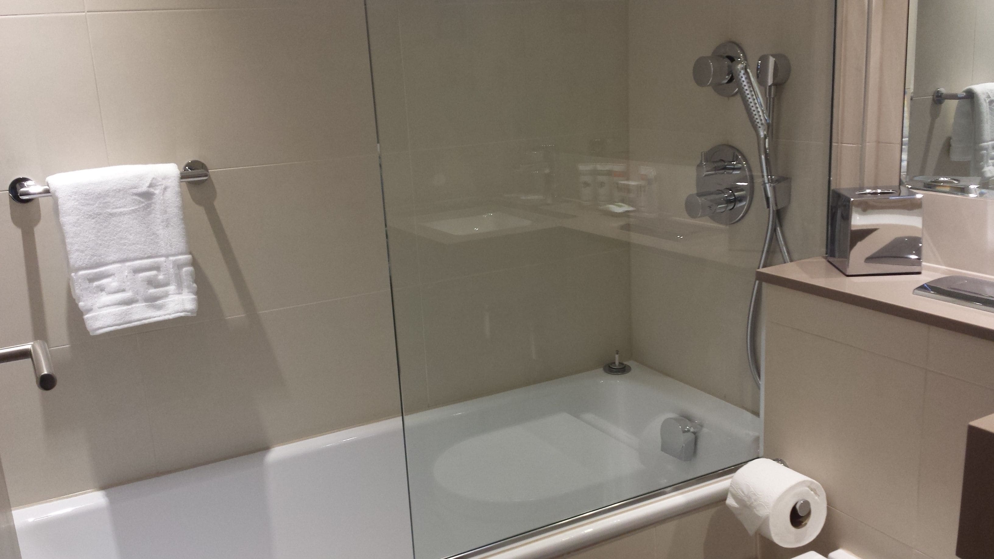 Een douche met glazen wanden, een wit ligbad, een handdoekhouder en een toiletrolhouder.