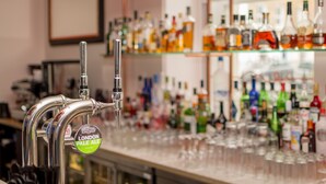 Eine Bar mit einem Zapfhahn, beschriftet mit „London Pale Ale“, und Regalen voller verschiedener Flaschen.