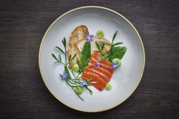 A plate with a slice of salmon, a piece of toast, and some green leaves and flowers.