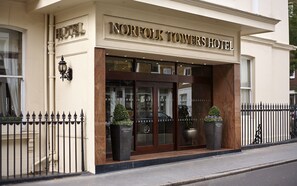 Het uiterlijk van Hotel Norfolk Towers, met een opvallende ingang, grote ramen en twee potplanten bij de entree.