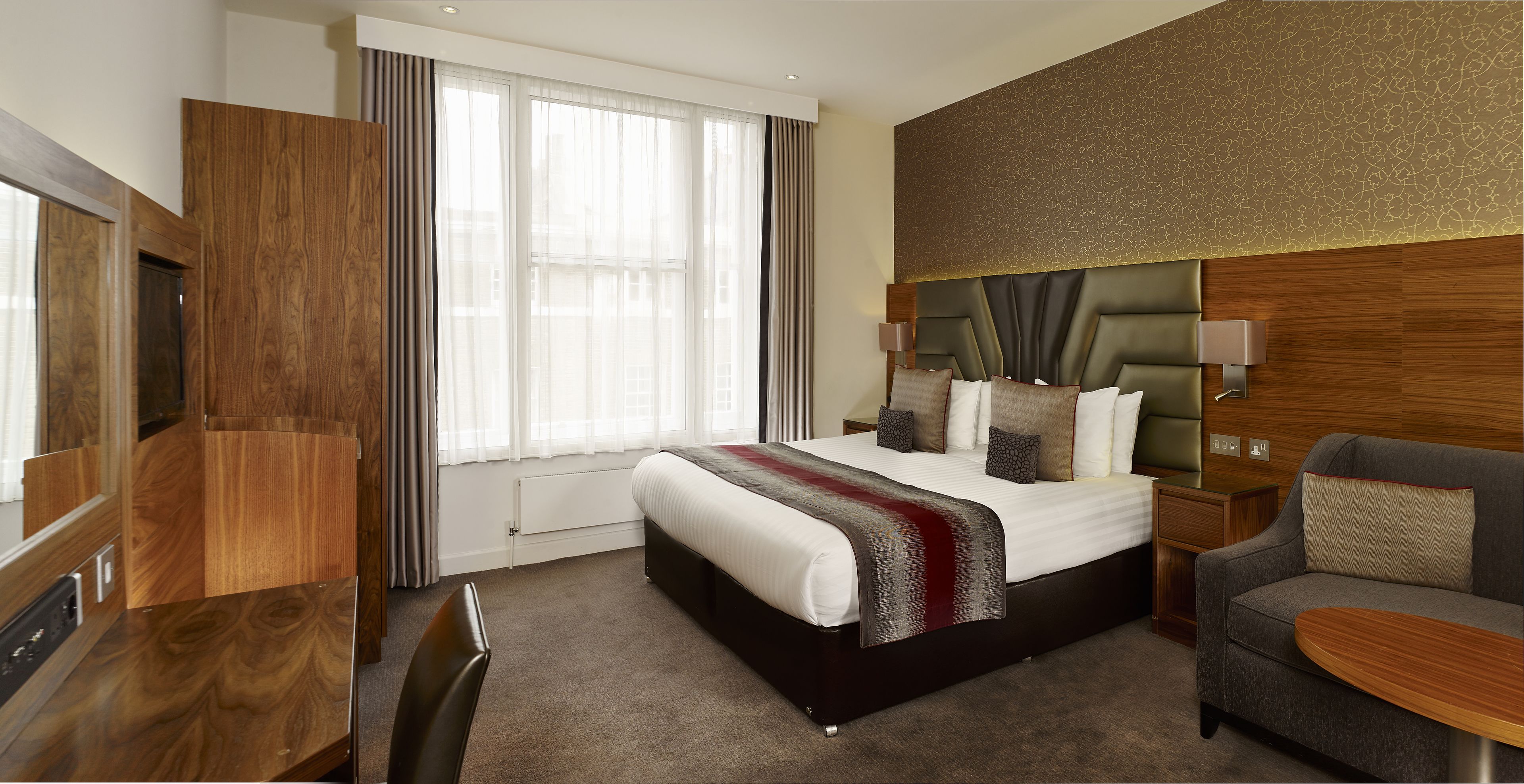 A hotel room with a large bed, a sofa, a TV, and a desk.