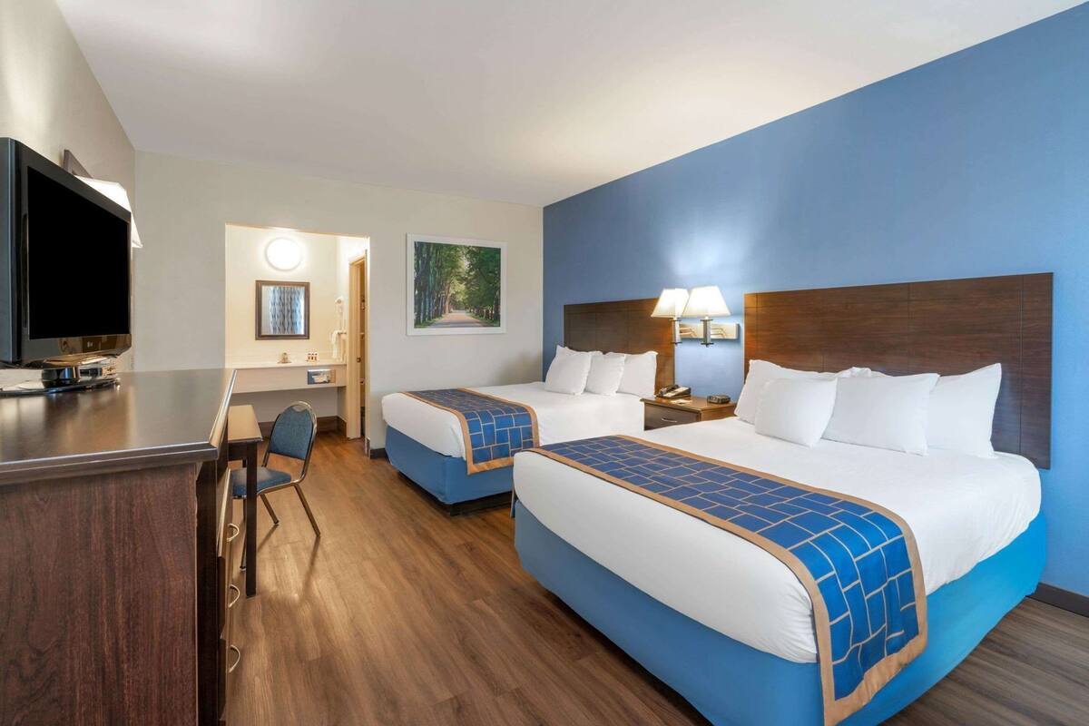 A hotel room with two beds, a desk, a TV, and a painting on the wall.