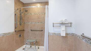 A walk-in shower with a glass door, a grab bar, a wheelchair-accessible bench, and a towel rack with towels.
