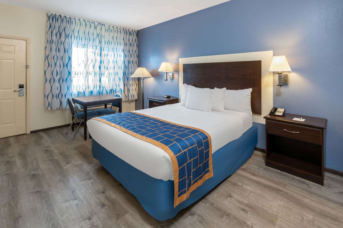 A hotel room with a bed, desk, and two bedside lamps.