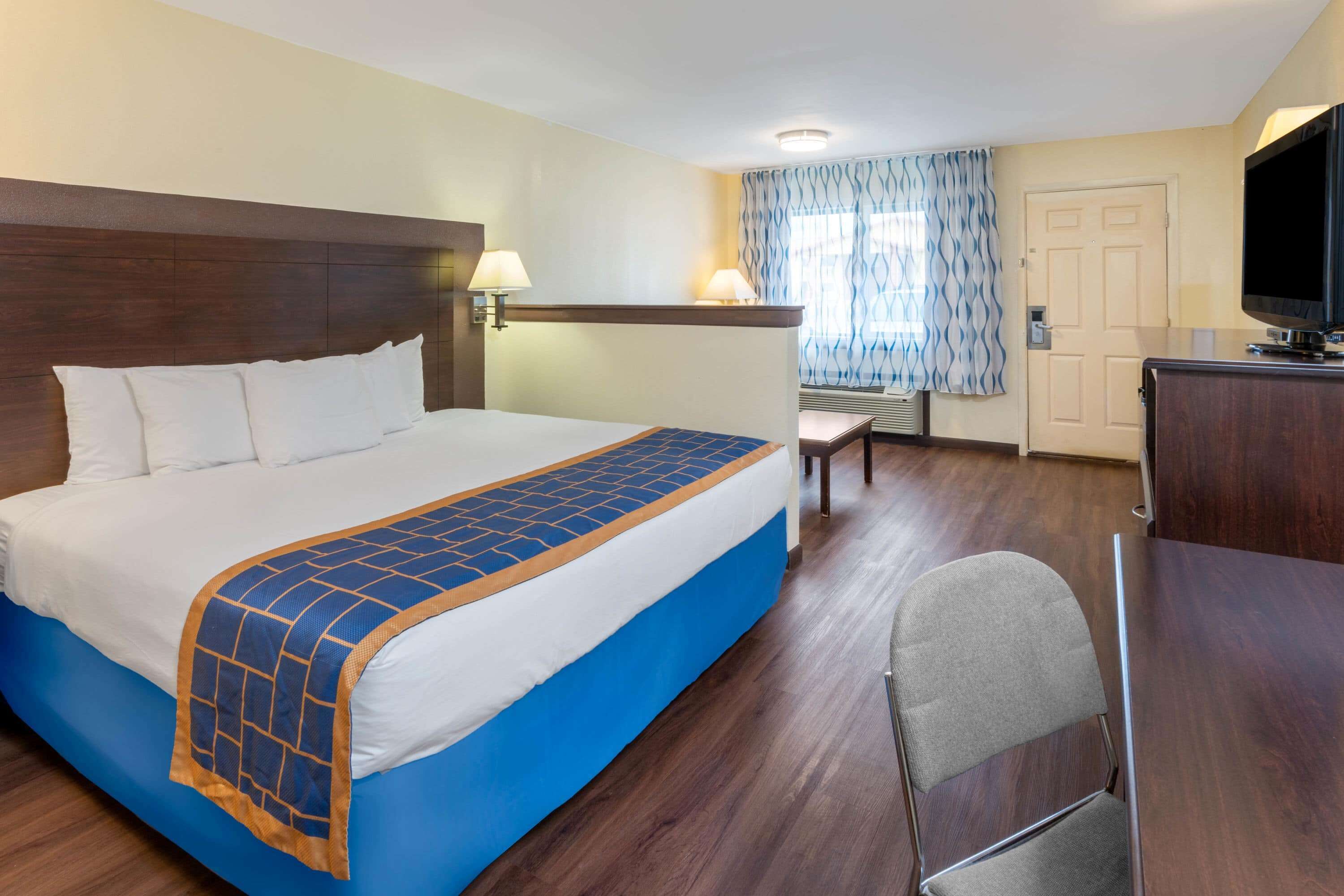 A hotel room with a large bed, a desk, a chair, a television, and a window with curtains.