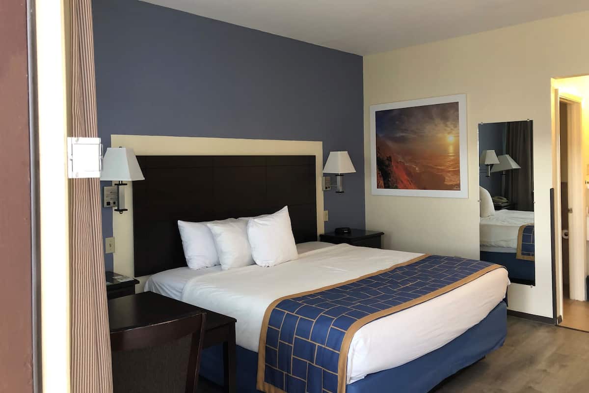 A hotel room with a bed, a desk, a chair, a nightstand, and a painting on the wall.