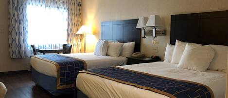 A hotel room with two beds, a desk, a chair, a lamp, and a nightstand with a phone.