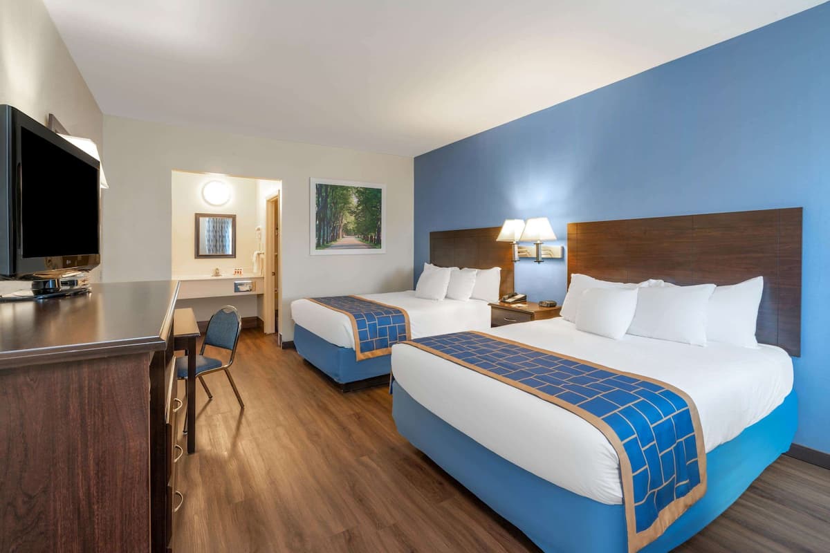 A hotel room with two beds, a desk, a TV, and a bathroom.