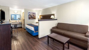 Ein Hotelzimmer mit Bett, einer Sitzecke, einem Schreibtisch mit Stuhl, einem Fernseher und einem Gemälde an der Wand.