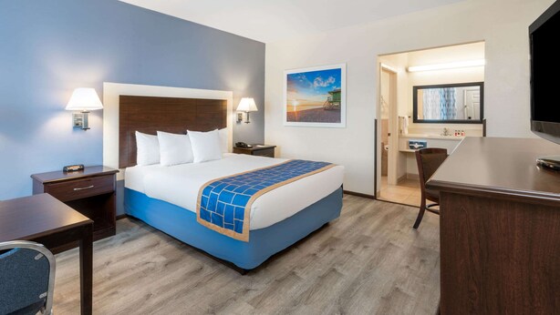 Ein Hotelzimmer mit Bett, Nachttischen, Schreibtisch, Stuhl, Fernseher und einem durchgegangenen Tür erkennbaren Badezimmer.