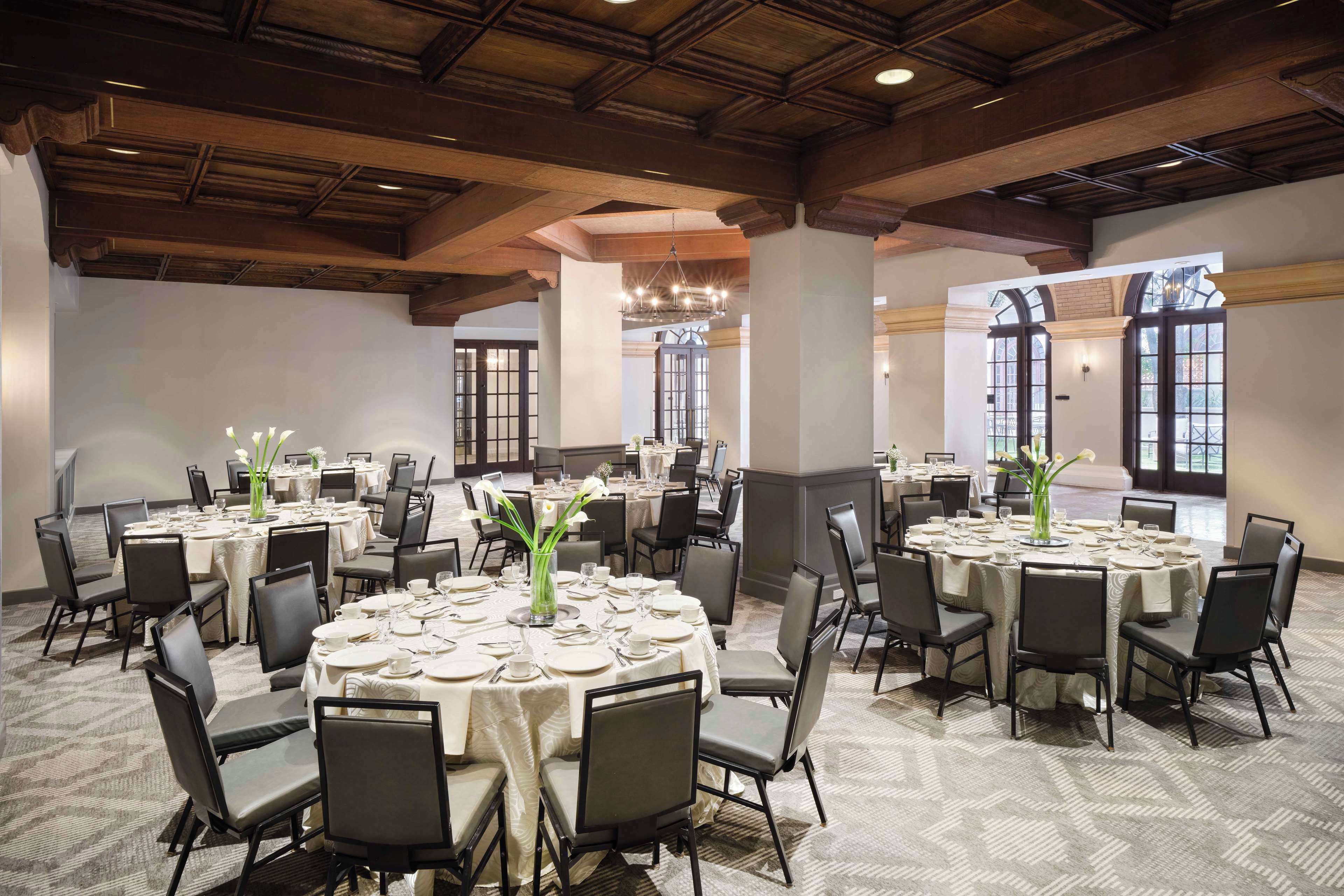 A large conference room with multiple round tables, each set with white tablecloths, chairs, and vases of flowers.