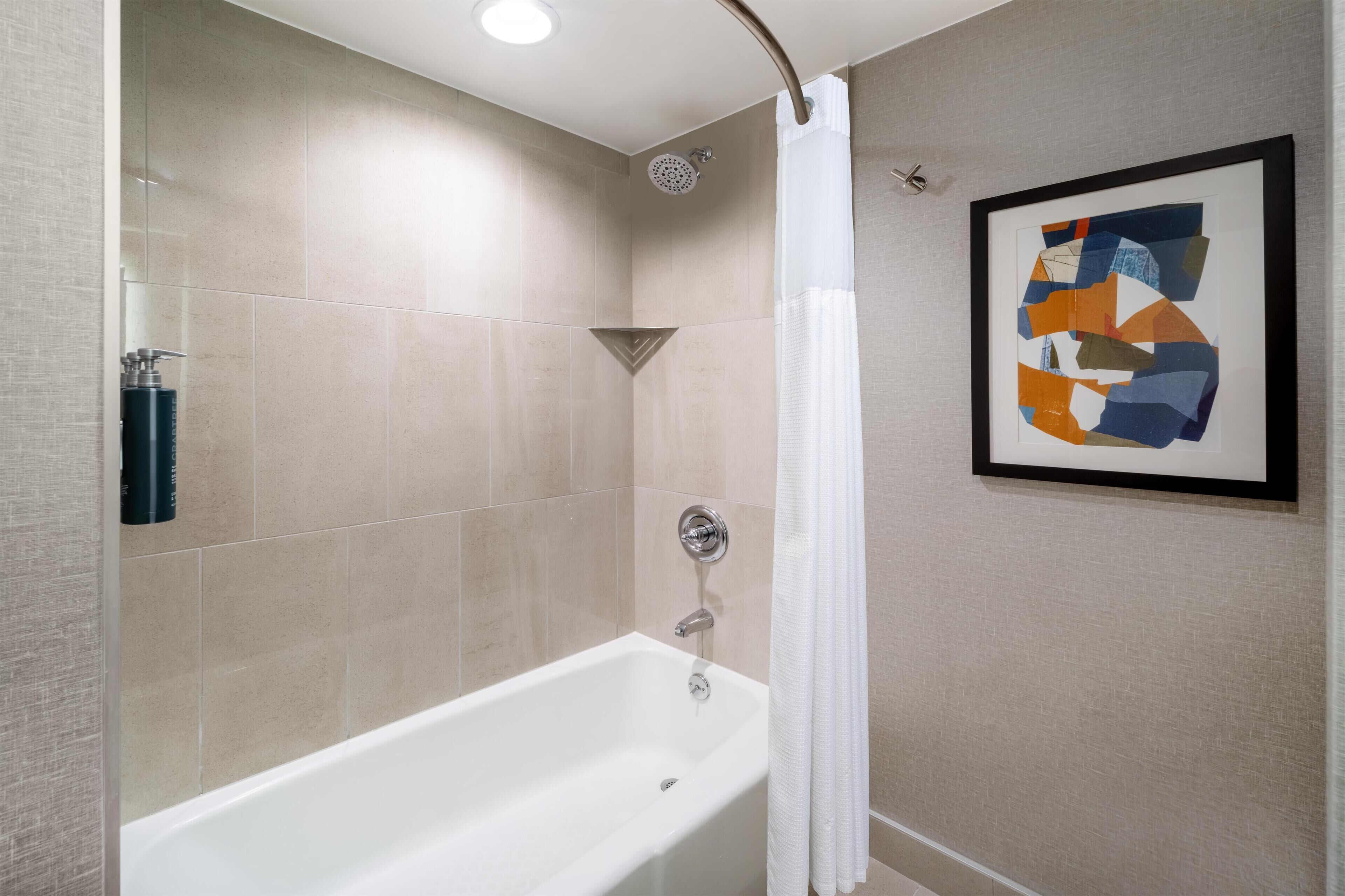 Une salle de bain moderne avec une baignoire, une douche et un tableau abstrait encadré.