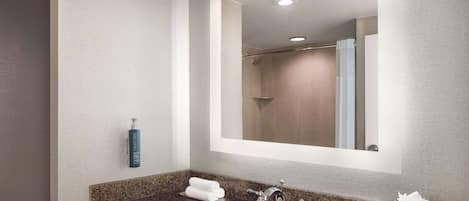 A bathroom with a granite countertop, a white sink, a mirror, a towel rack, and a shower area.