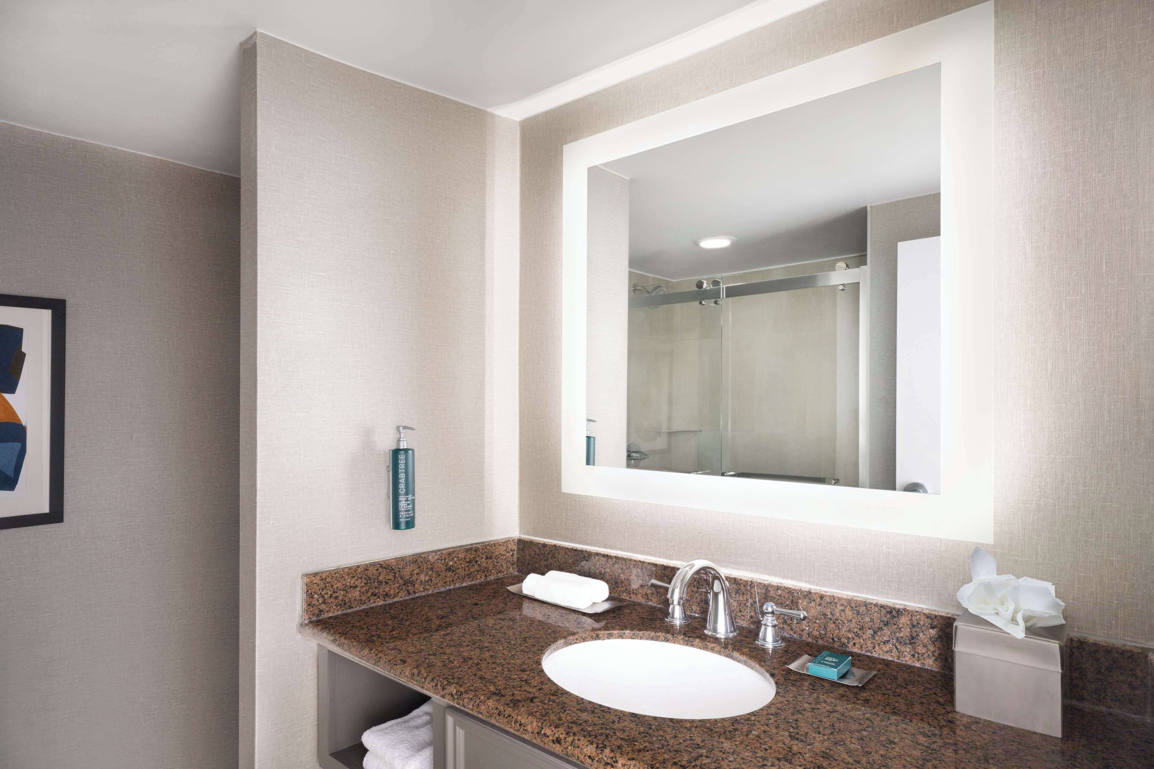 Un baño de hotel con lavamanos de encimera de granito, un espejo grande y un perchero para toallas.