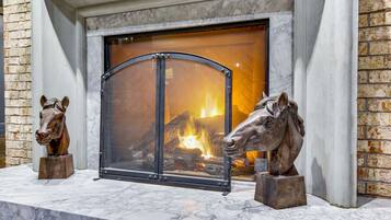 Una chimenea con una reja de metal, flanqueada por dos estatuas de caballos sobre un repisa de mármol.