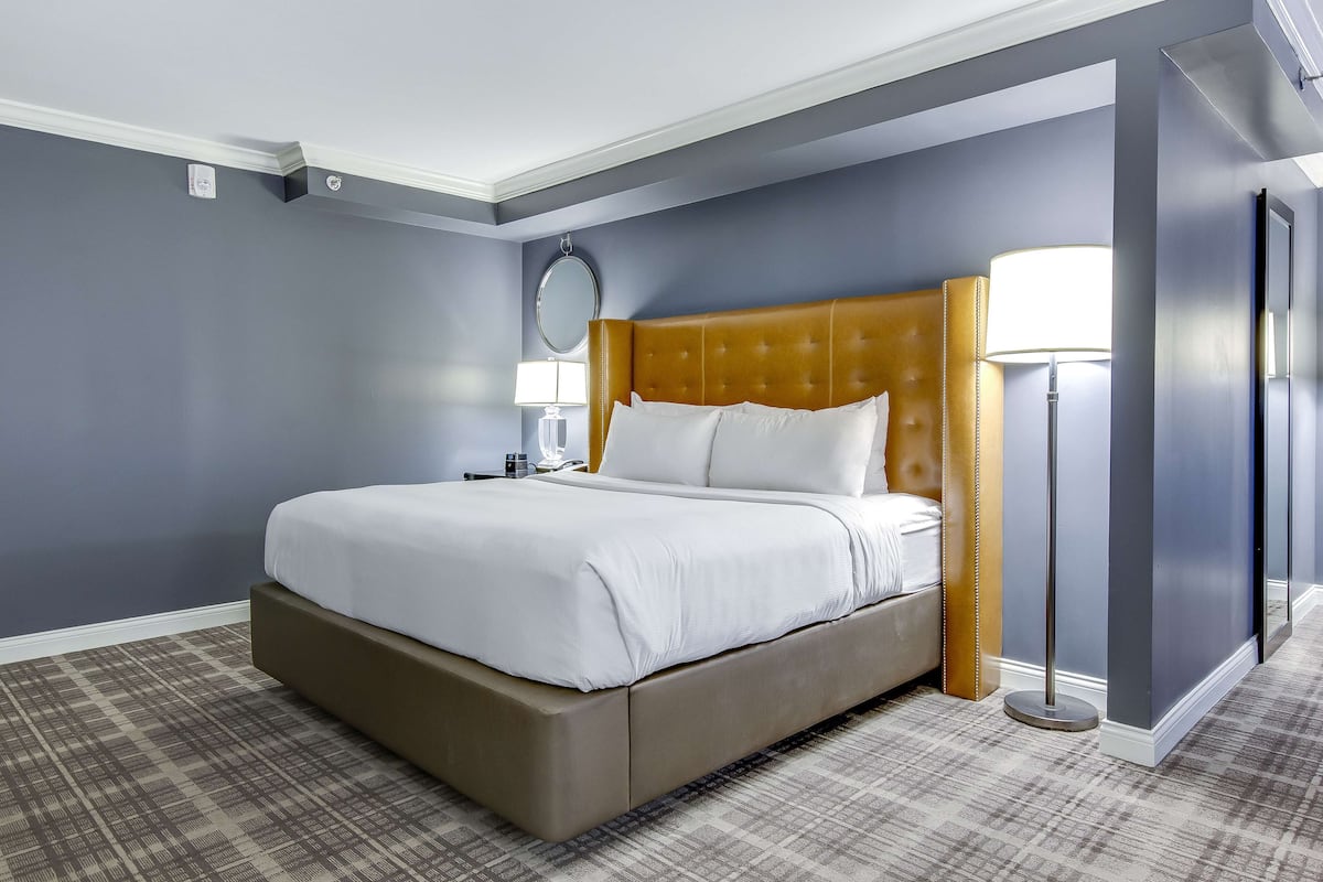 Una habitación de hotel con una cama grande, una mesita de noche, una lámpara y un espejo.