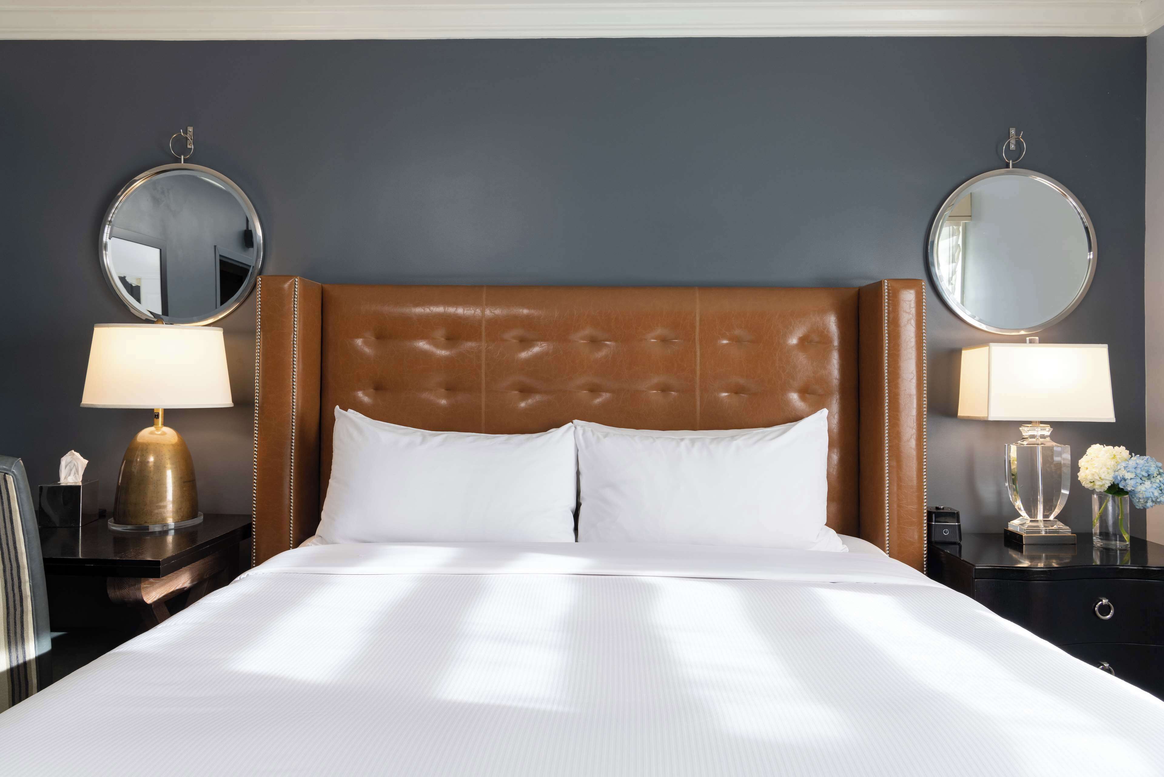 A hotel room with a large bed, two bedside tables with lamps, and two wall-mounted mirrors.