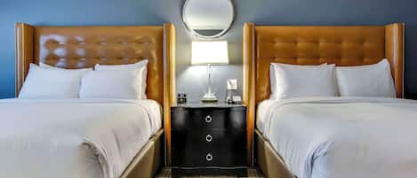 A hotel room with two beds, a nightstand with drawers, a round mirror, and a bedside lamp.
