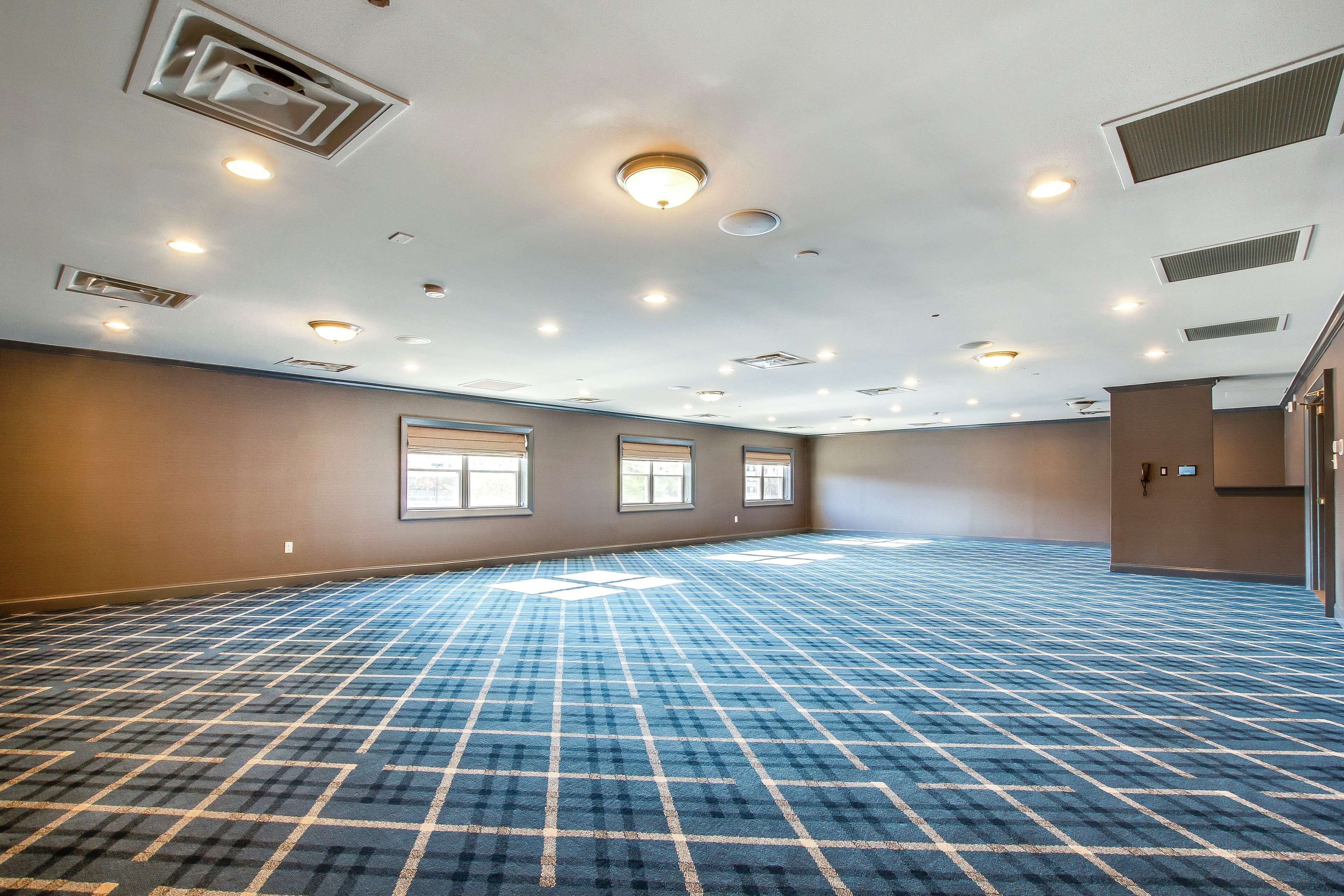 A large, empty conference room with a blue patterned carpet, multiple windows, and recessed ceiling lights.