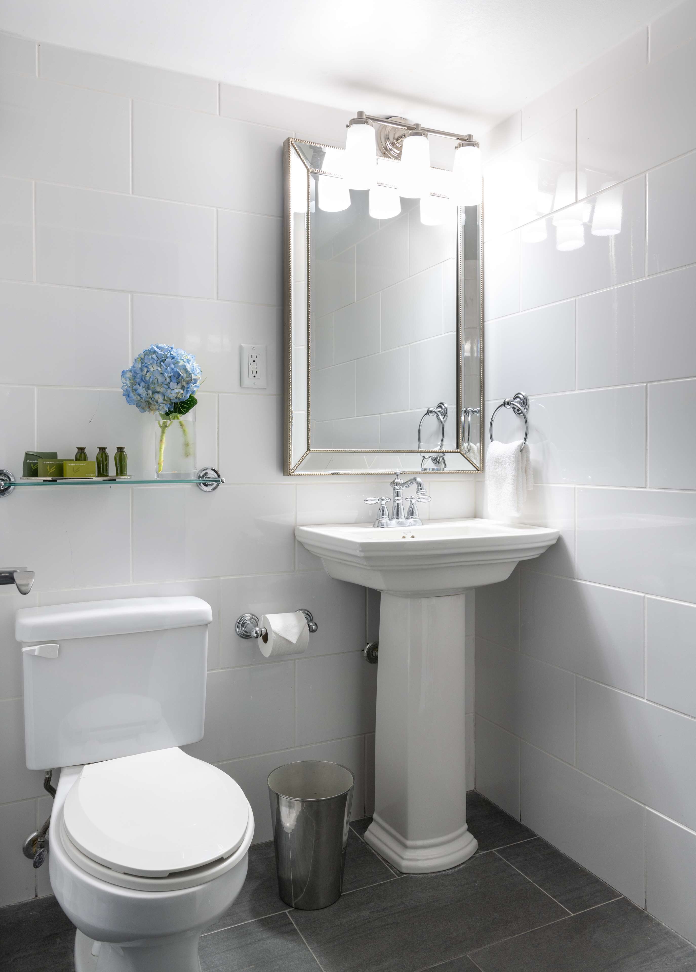 Un baño moderno con inodoro blanco, lavamanos pedestal y un espejo grande con iluminación.