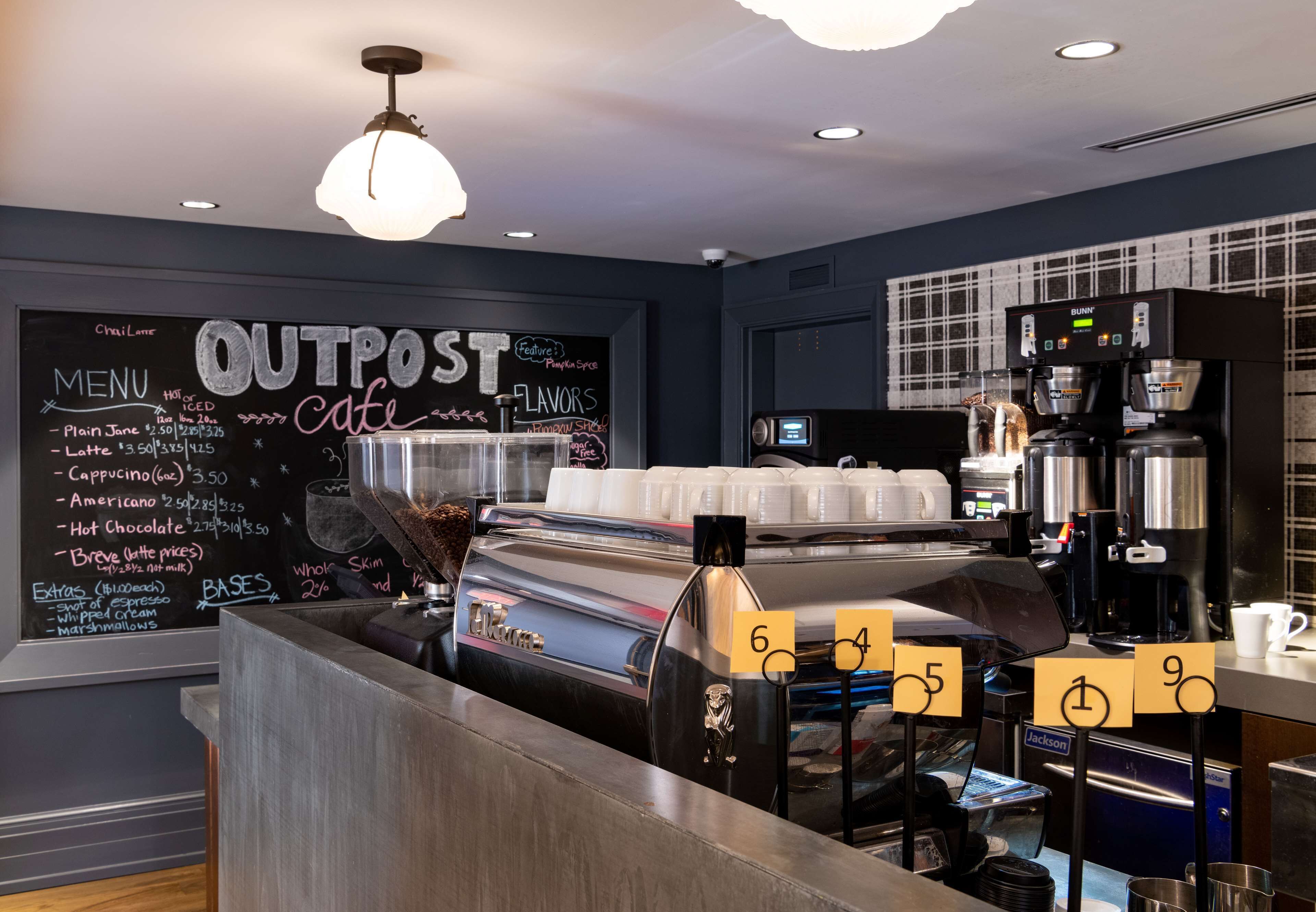 Interior de una cafetería con un menú en pizarra, máquinas de espresso y una barra.