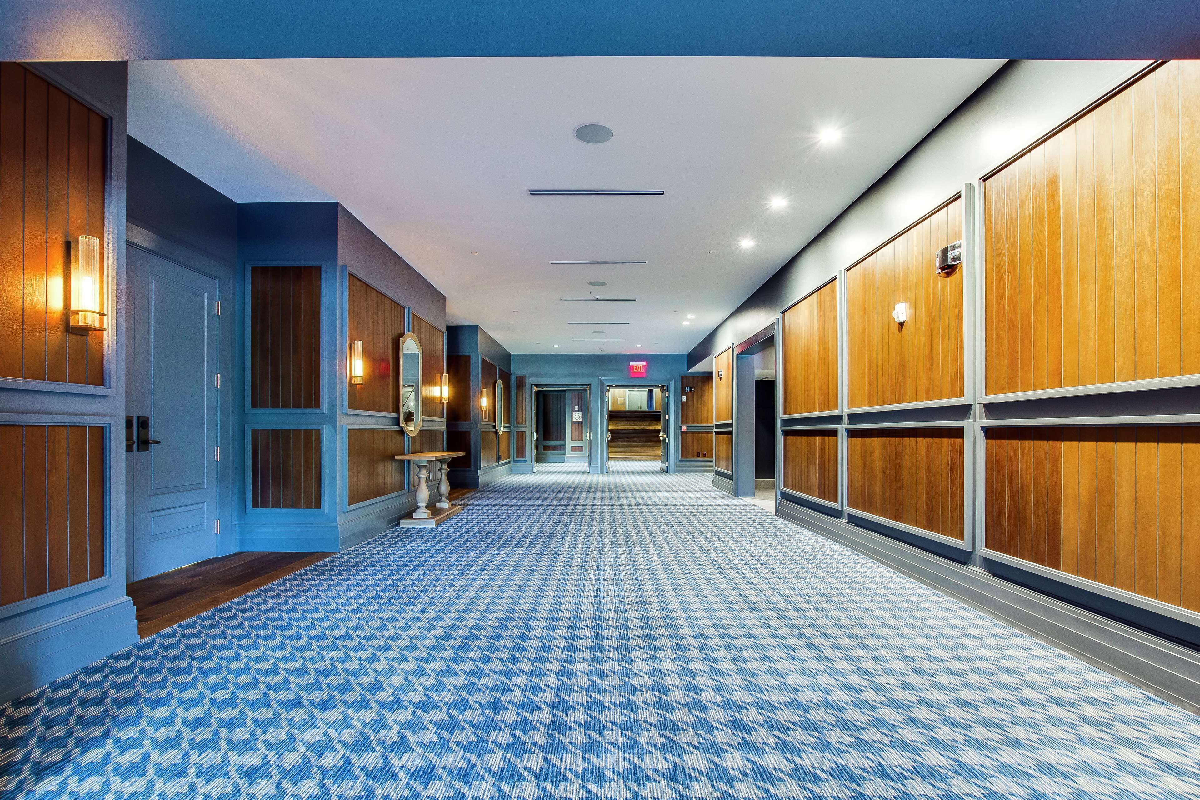 A hotel hallway with blue walls, wooden paneling on the doors, and a patterned carpet.