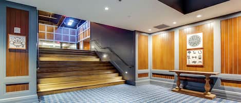 Vestíbulo de hotel con suelo a cuadros, paneles de madera, una escalera y una recepción.