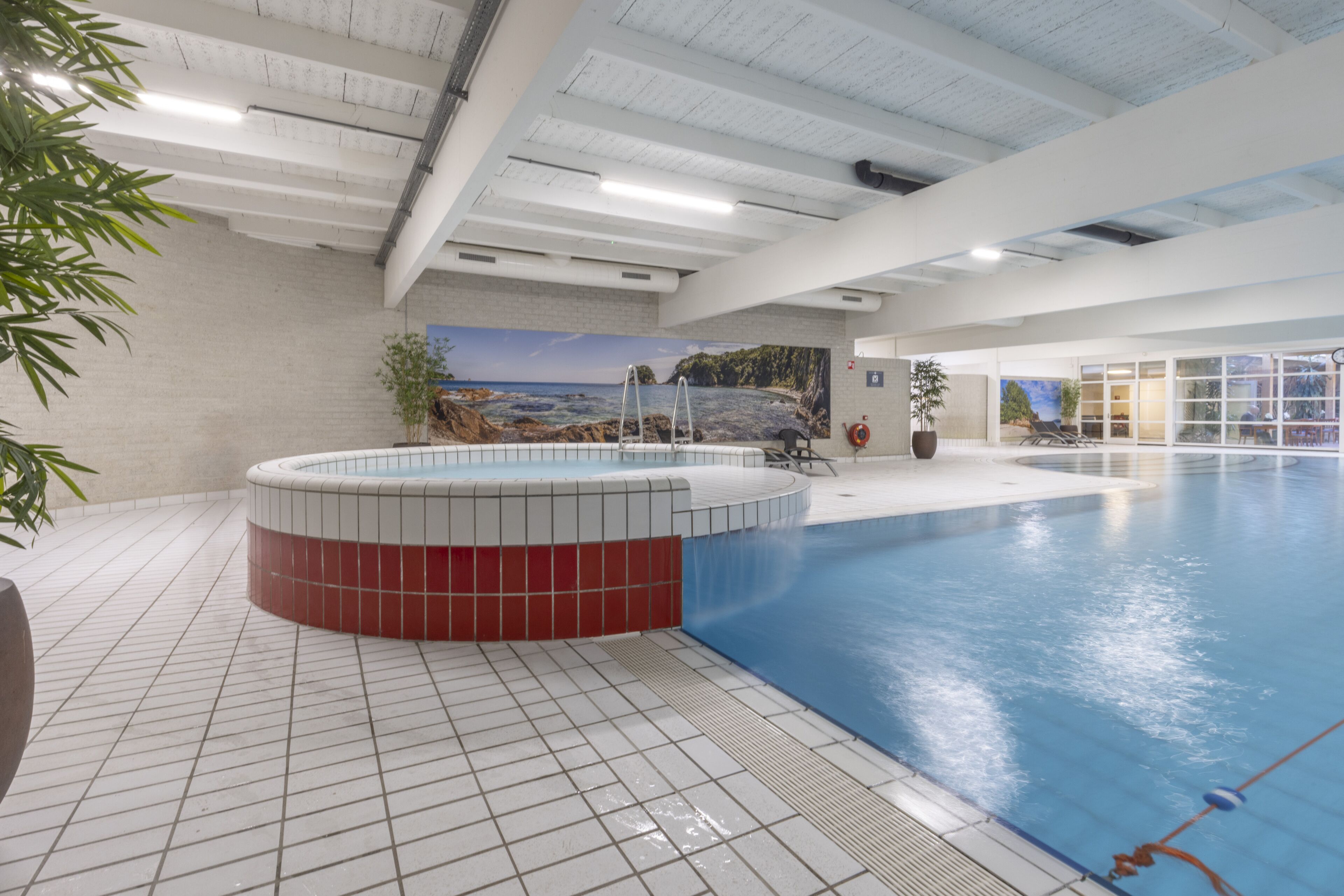 Una piscina interna con vasca idromassaggio, pavimento piastrellato e un affresco con una veduta costiera.