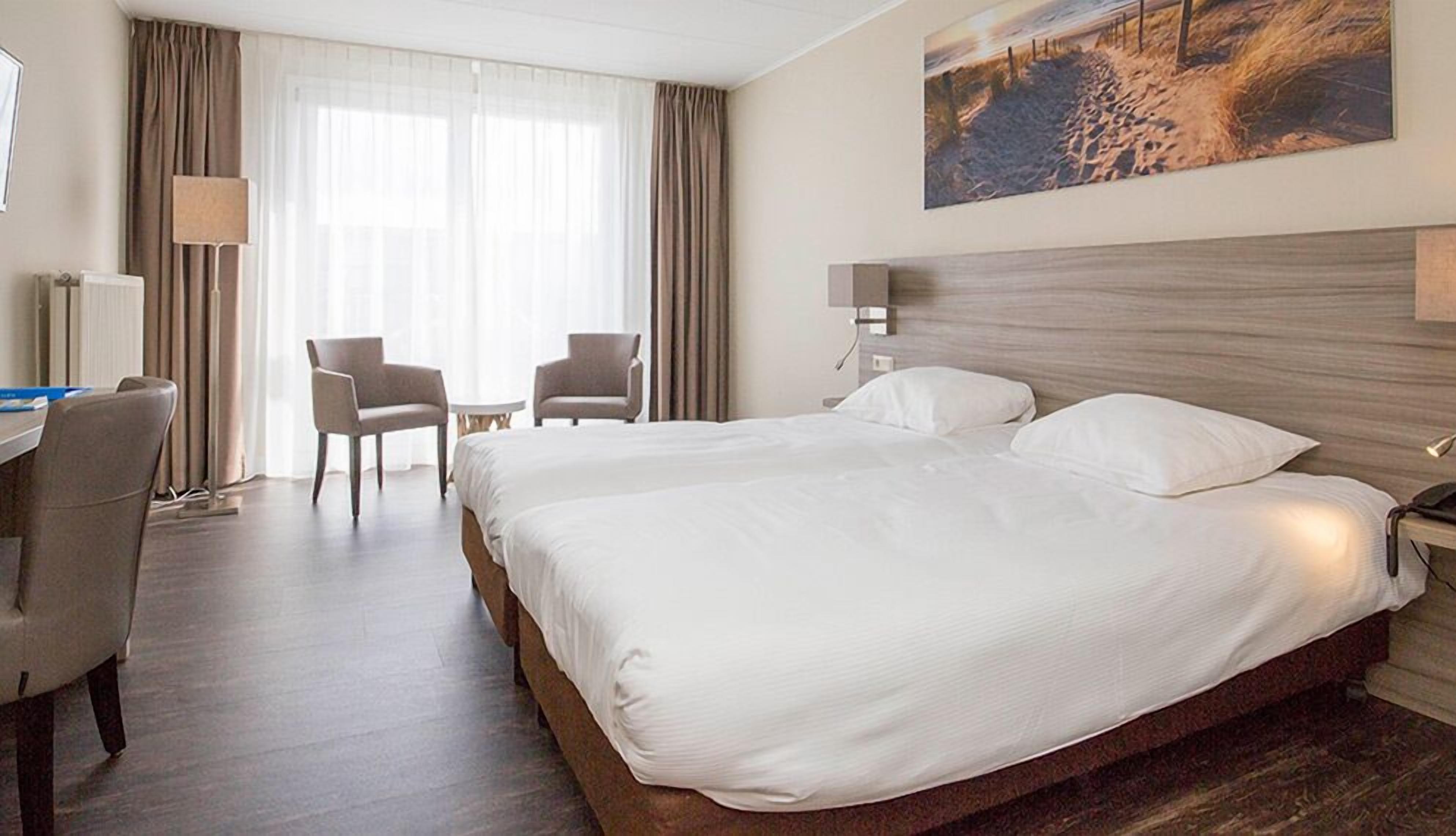 Ein Hotelzimmer mit einem großen Bett, zwei Sesseln, einem Schreibtisch und einem Bild an der Wand.