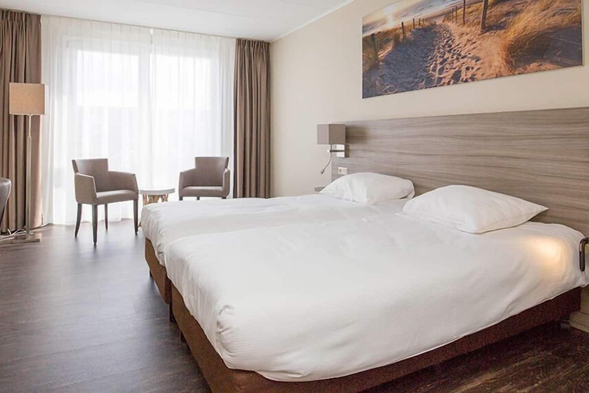 A hotel room with a large bed, two chairs, a desk, and a painting on the wall.