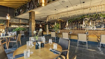 A restaurant with a wooden table set for dining, hanging lights, and a bar area.