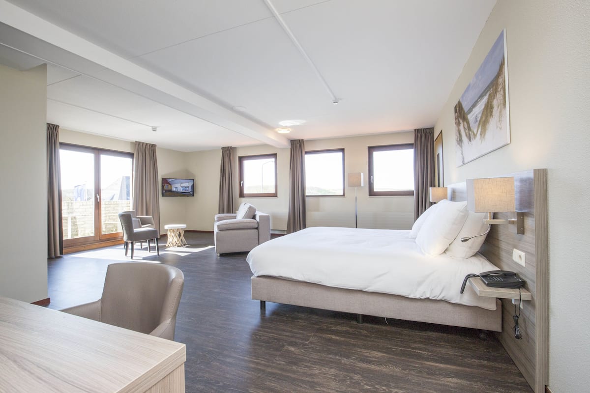 A hotel room with a large bed, a desk, a chair, and a television on the wall.