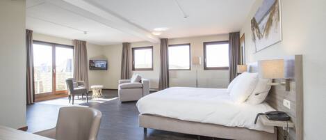 A hotel room with a large bed, a desk, a chair, and a television on the wall.