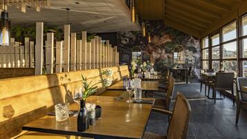 Un restaurante con mesas y sillas de madera, y un techo alto con luces colgantes.