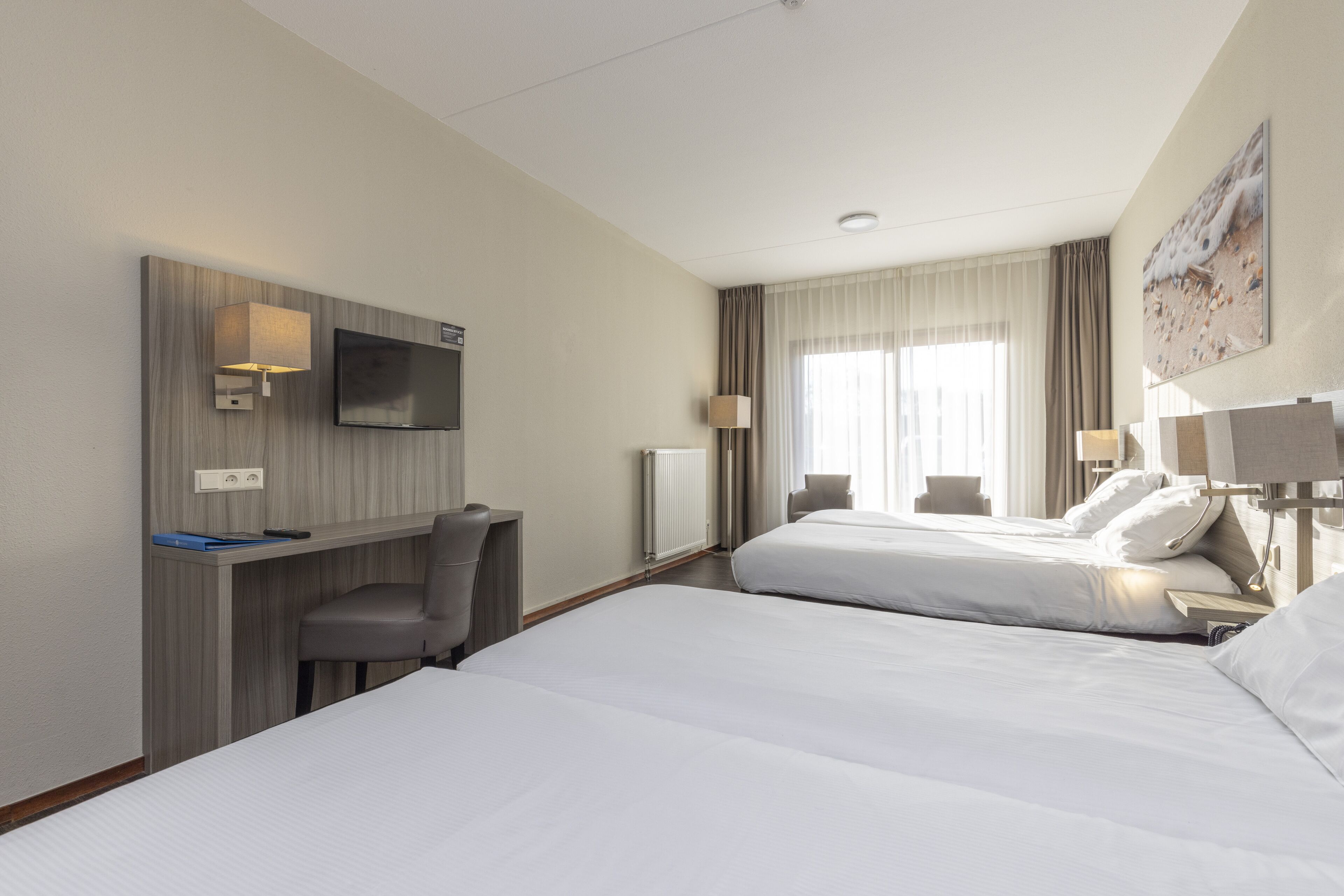 Une chambre d’hôtel avec deux lits, un bureau, une chaise, une télévision et une fenêtre avec des rideaux.