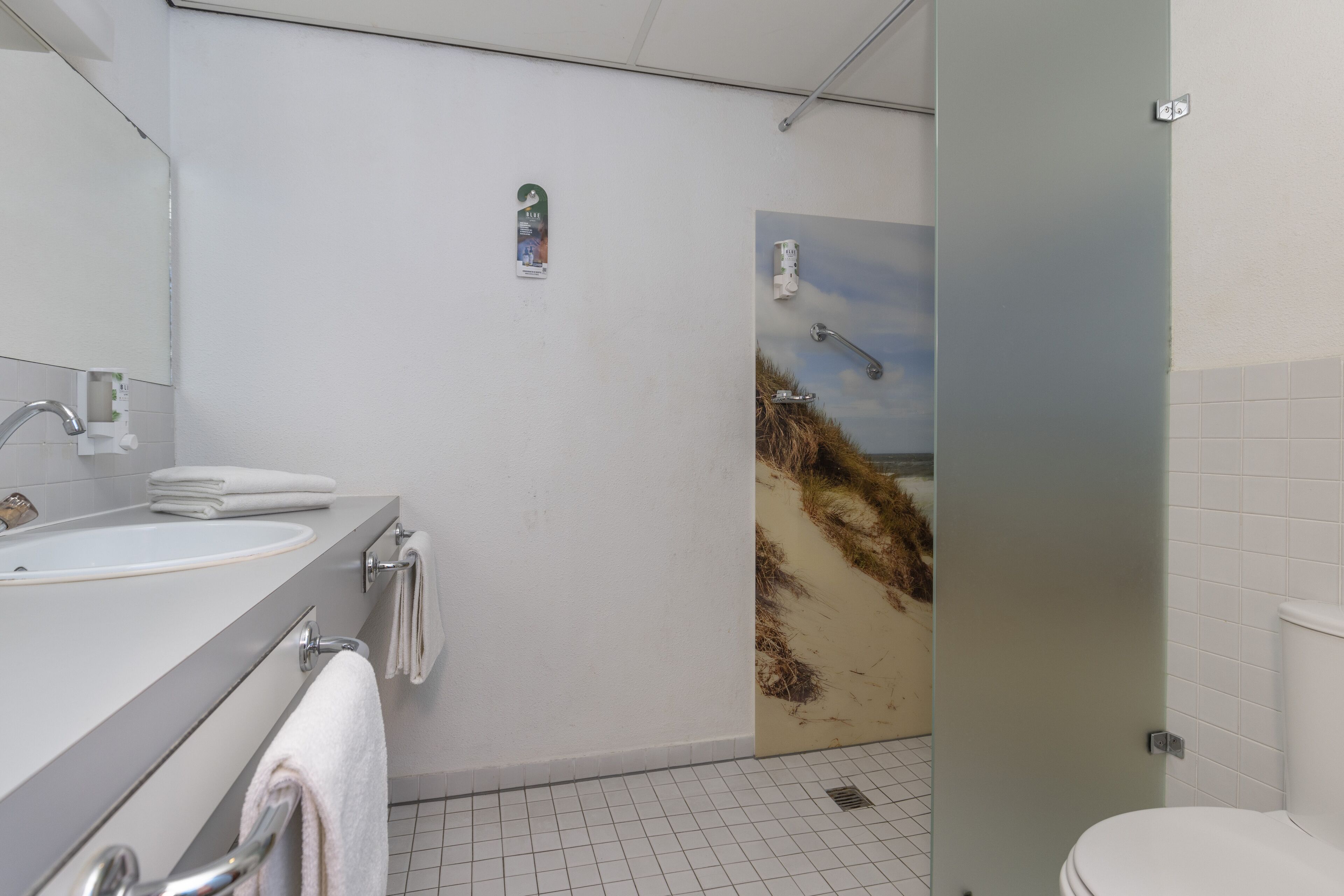 A bathroom with a sink, mirror, and a shower with a beach mural.