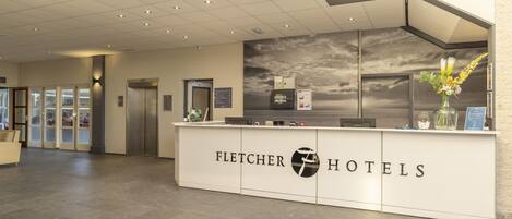 A reception desk with the Fletcher Hotels logo, a modern interior with a tiled floor, and a large window with a view of the sky.