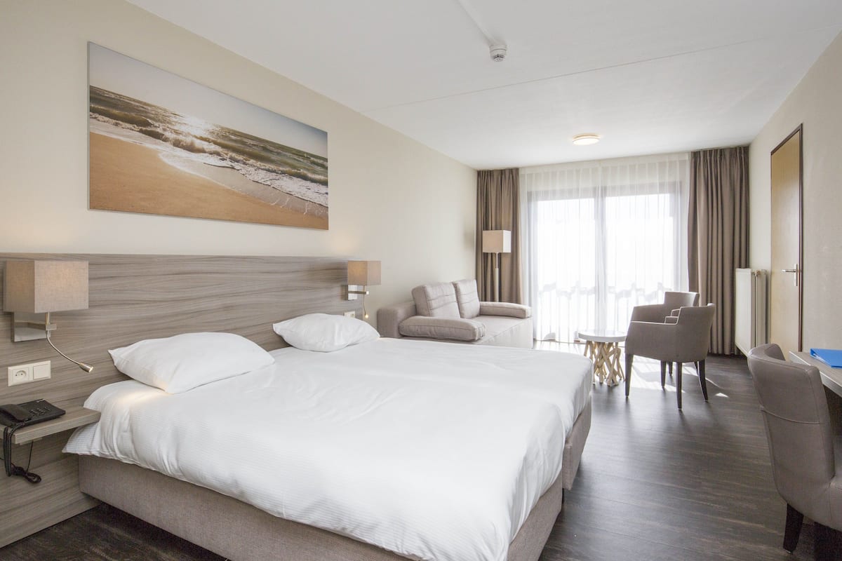 A hotel room with a large bed, a desk with a chair, a sofa, and a painting of a beach scene.