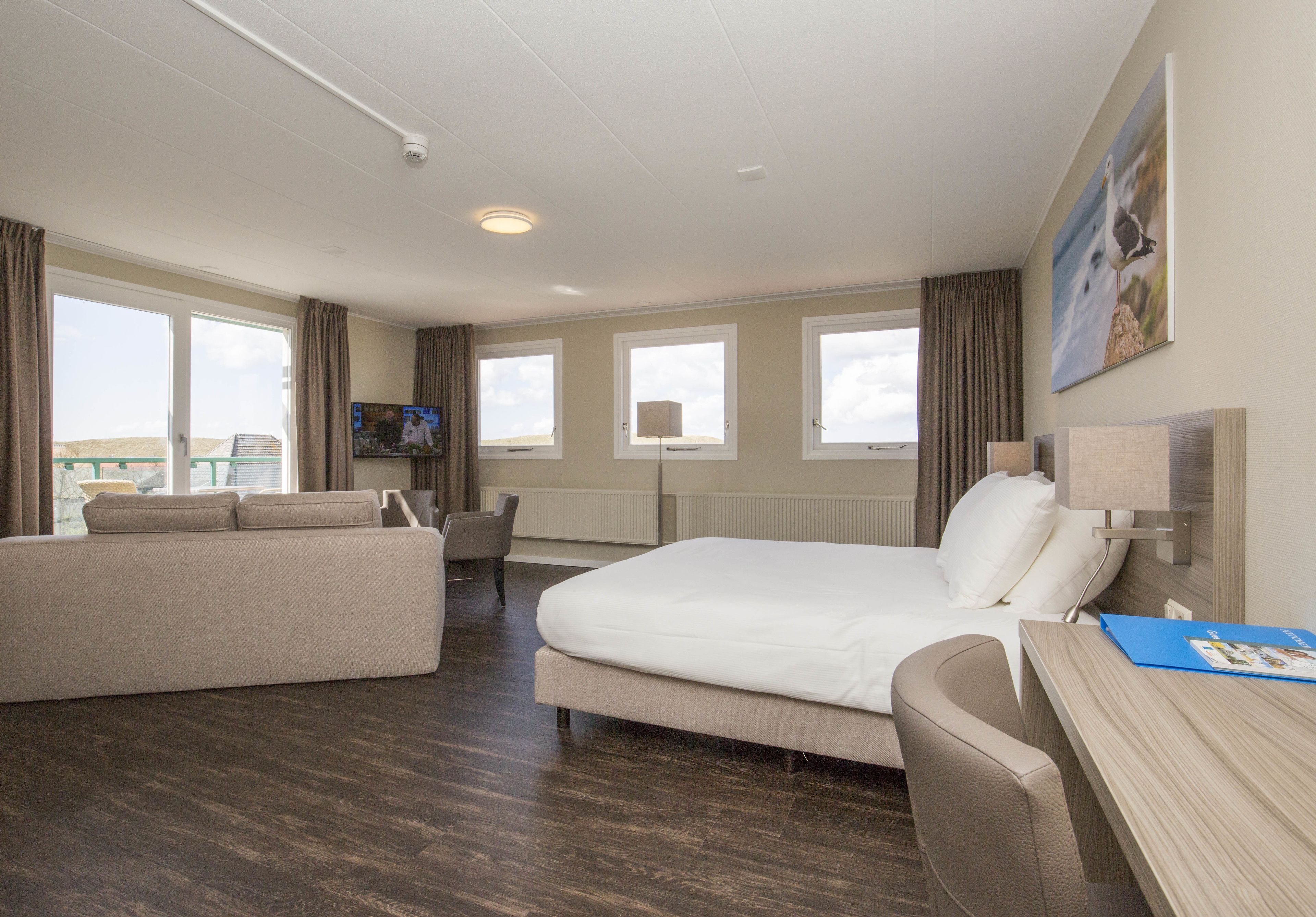 A hotel room with a bed, a sofa, a desk, and a TV.