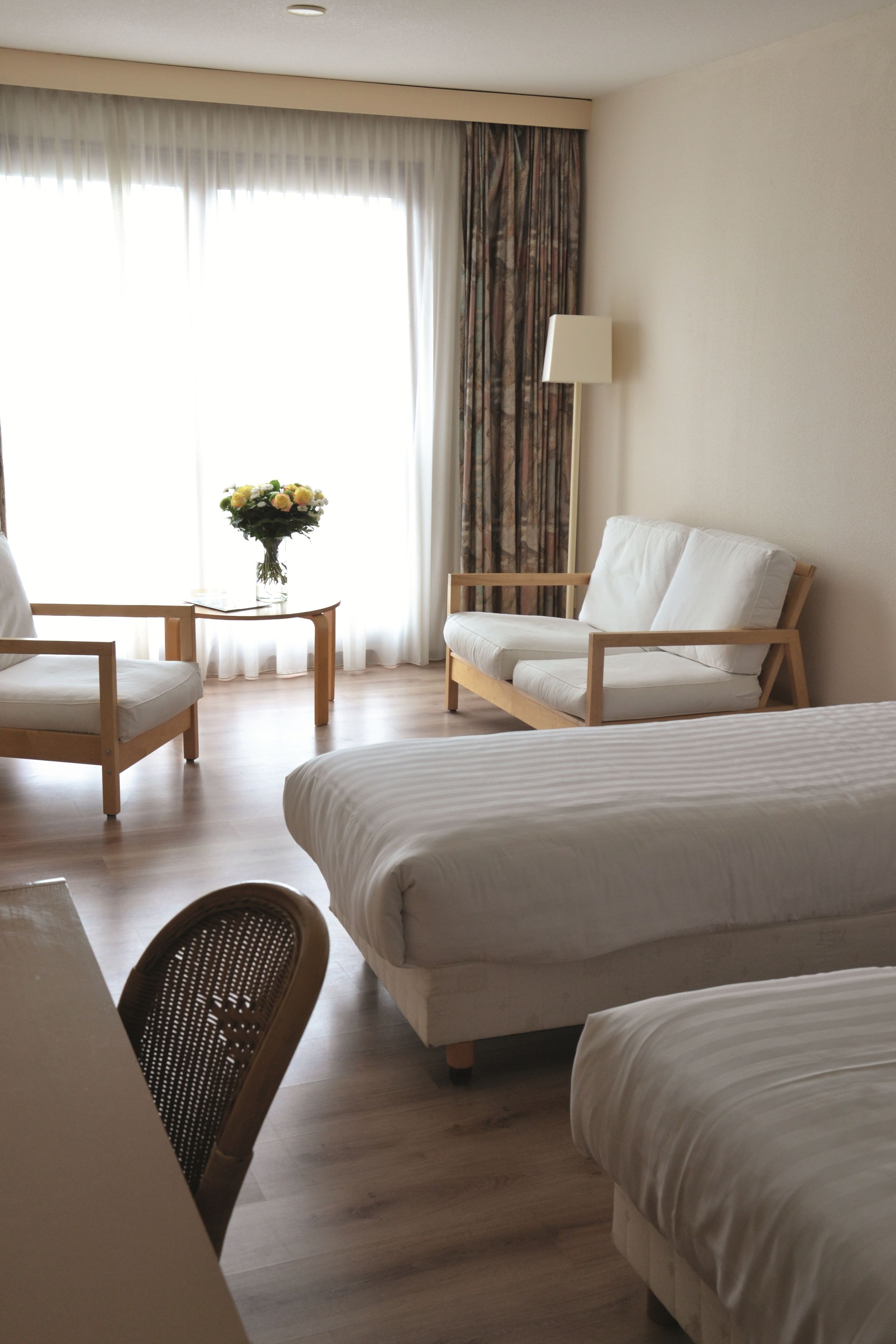 A hotel room with two beds, a wooden chair, a small table, and a lamp.