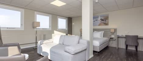 A modern hotel room with a sofa, a bed, a desk, and a chair.