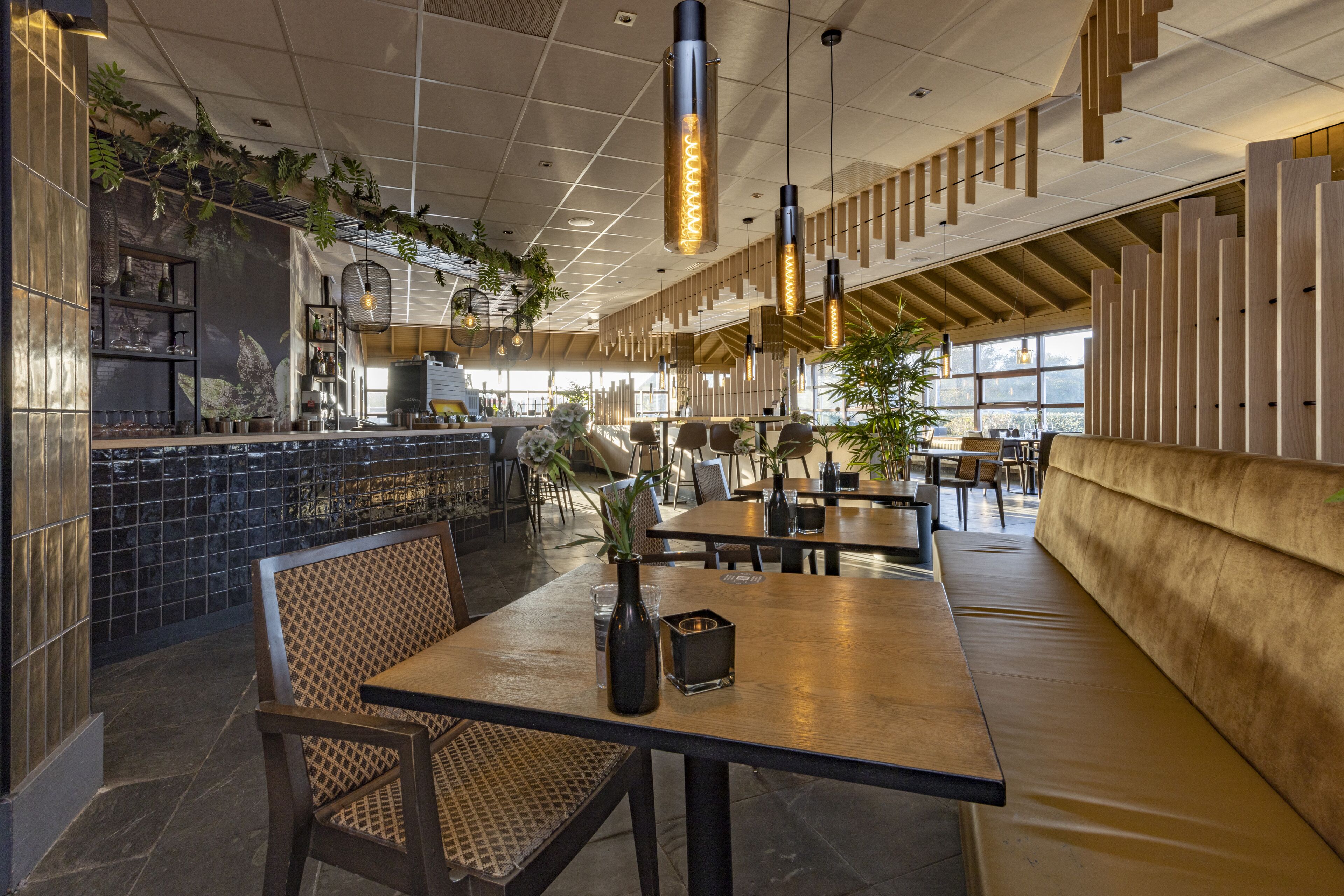 A modern restaurant interior with high ceilings, pendant lighting, and a mix of seating arrangements including tables and booths.