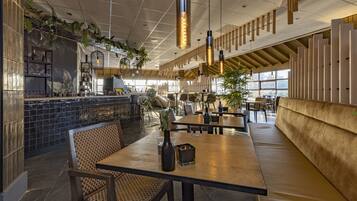 Interior moderno de restaurante com pé direito alto, luminárias pendentes e uma variedade de assentos, incluindo mesas e cabines.