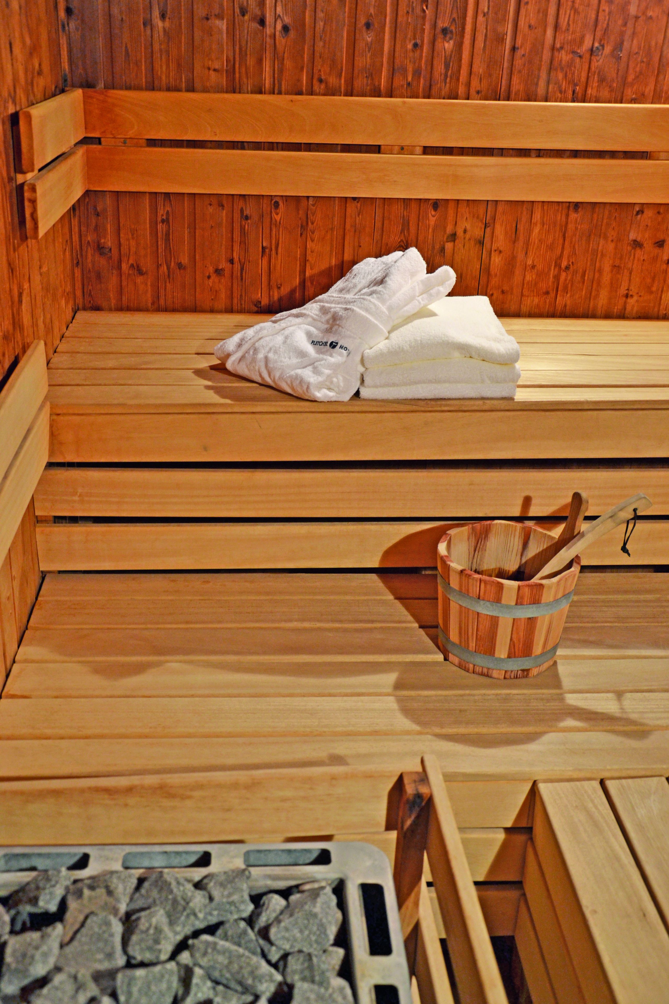 Uma sauna de madeira com bancos, toalhas e um balde de madeira com escova.