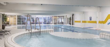 An indoor swimming pool with clear water, a diving board, and a tiled floor.