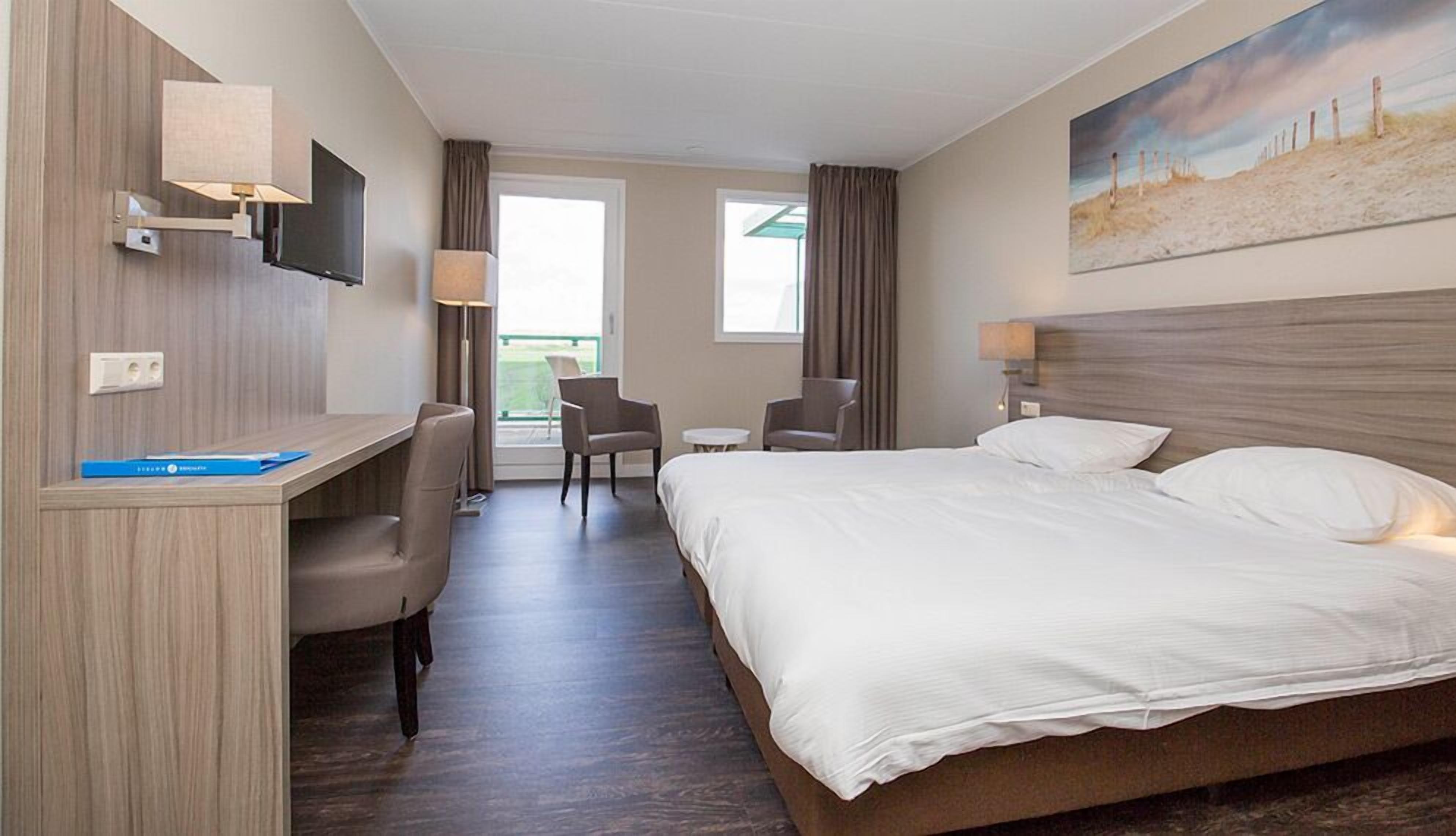 Ein Hotelzimmer mit Bett, Schreibtisch, Stühlen und einem Bild an der Wand.
