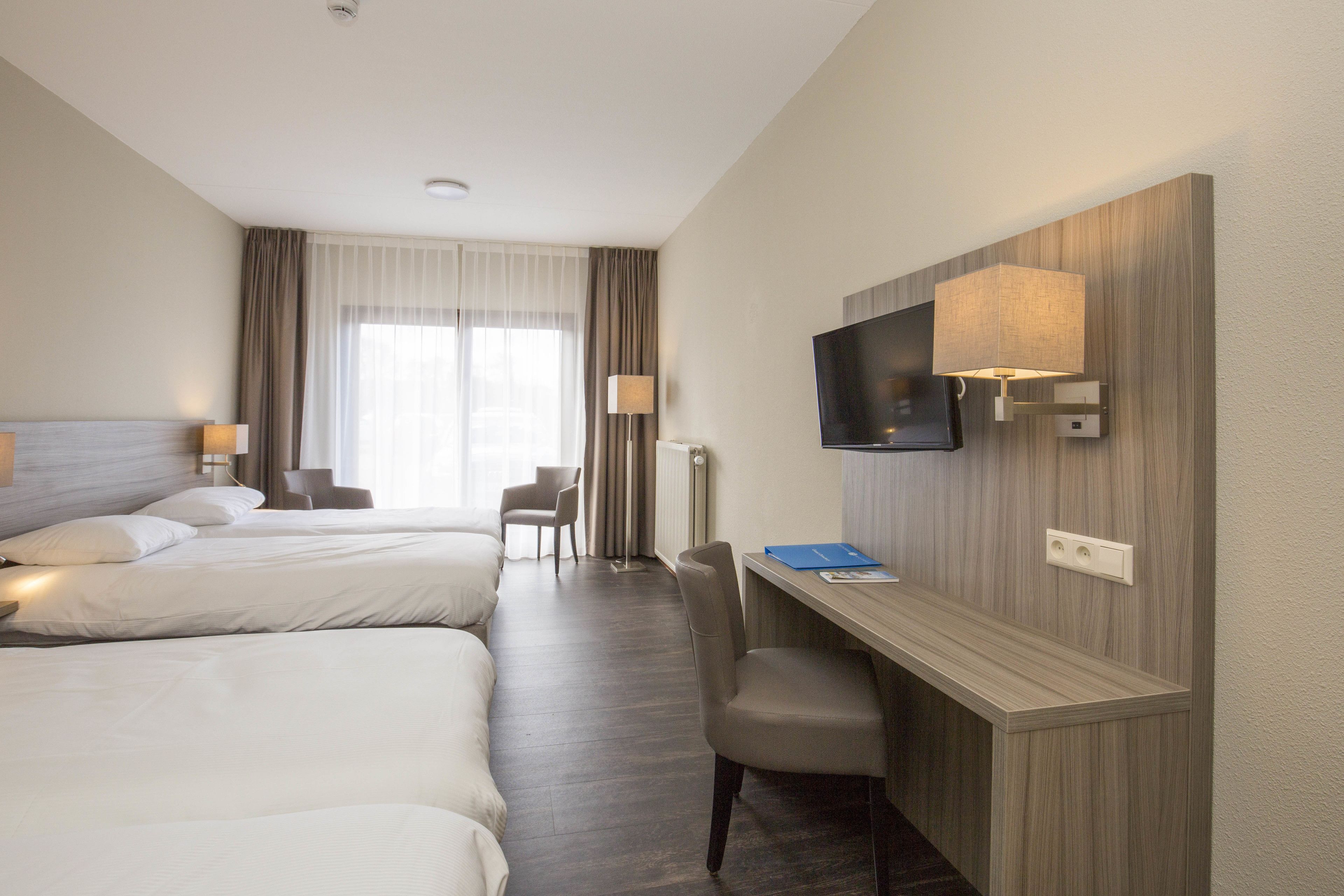 Une chambre d’hôtel avec deux lits, un bureau, une chaise, une télévision et une lampe.