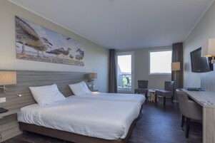 A hotel room with two beds, a desk, a chair, a TV, and a painting of birds on the wall.